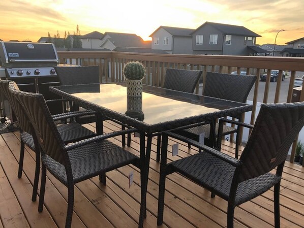 Um terraço com mesa retangular e seis cadeiras de vime, um arranjo de cactos e uma churrasqueira.