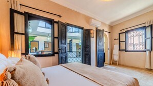 Quarto de hotel com cama, janela com cortinas, porta com detalhe decorativo e vista para o exterior.