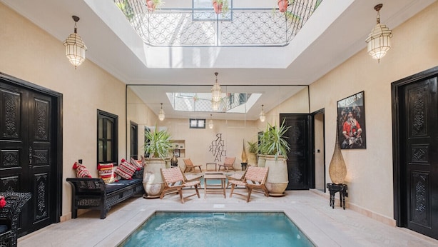 Uma área de piscina com teto de vidro, portas pretas e mobiliário com plantas em vasos.