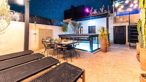 Uma área de refeições ao ar livre com mesa, cadeiras, um bar e uma planta de cacto.