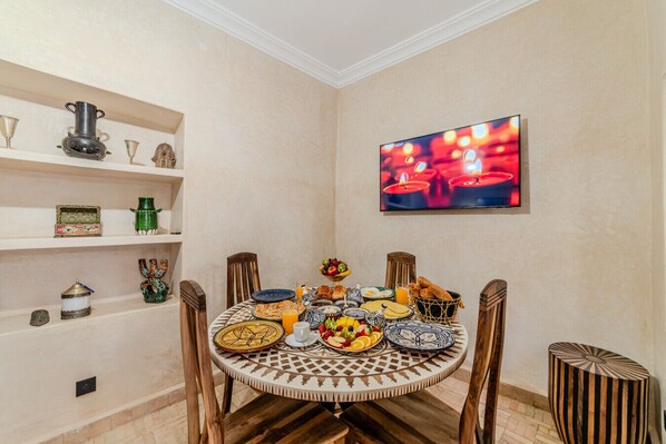 Un comedor con una mesa redonda dispuesta para una comida, rodeada de sillas de madera. Un televisor está montado en la pared sobre la mesa.