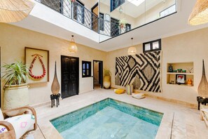 A spacious indoor pool area with a clear view of the sky, a black door, a patterned wall, and a small shelf with items.