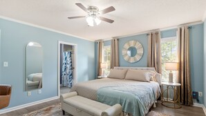 A bedroom with a bed, a bench, a round mirror, and a ceiling fan. - Fenced Yard | Pool Access | Fire Pit (Wake Forest)