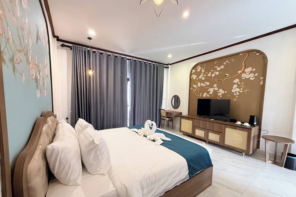 A hotel room with a large bed, a desk with a TV, and a decorative wall.