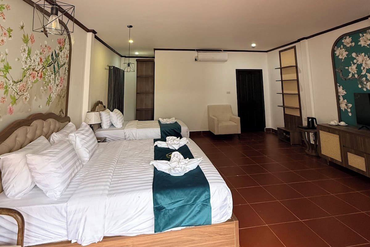 A hotel room with two beds, a sitting area, a TV, and a decorative wall.