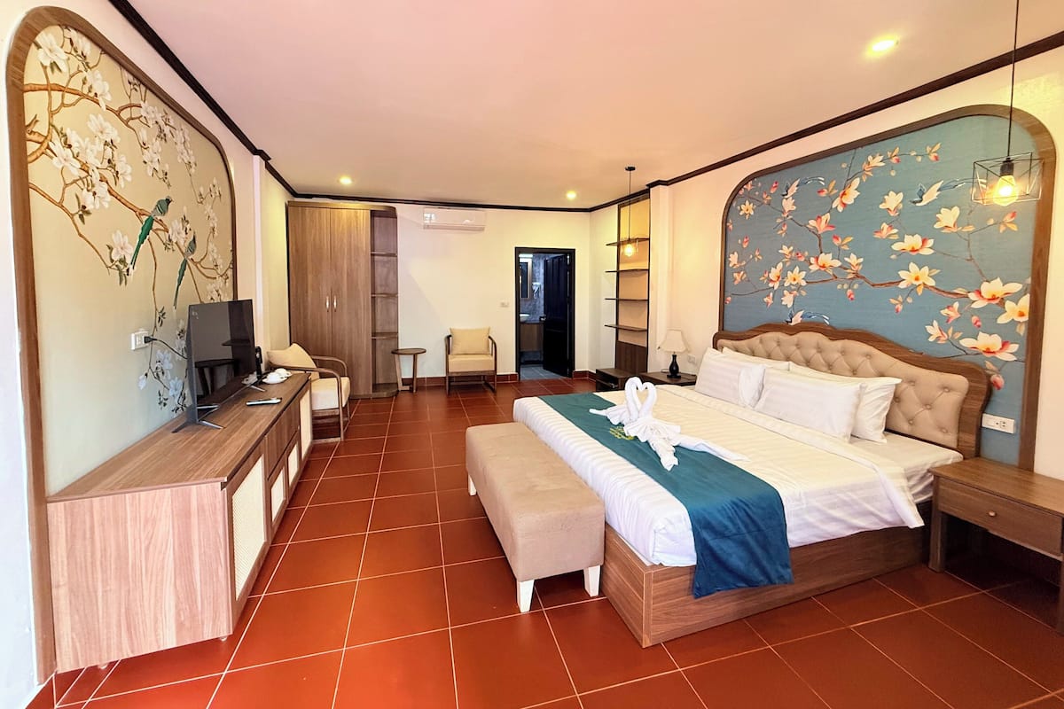A hotel room with a large bed, a desk with a computer, a chair, a small table, and a wardrobe.