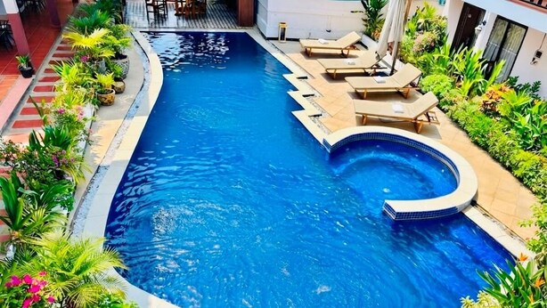 Una piscina a forma di curva, circondata da piante in vaso e sedie a sdraio.