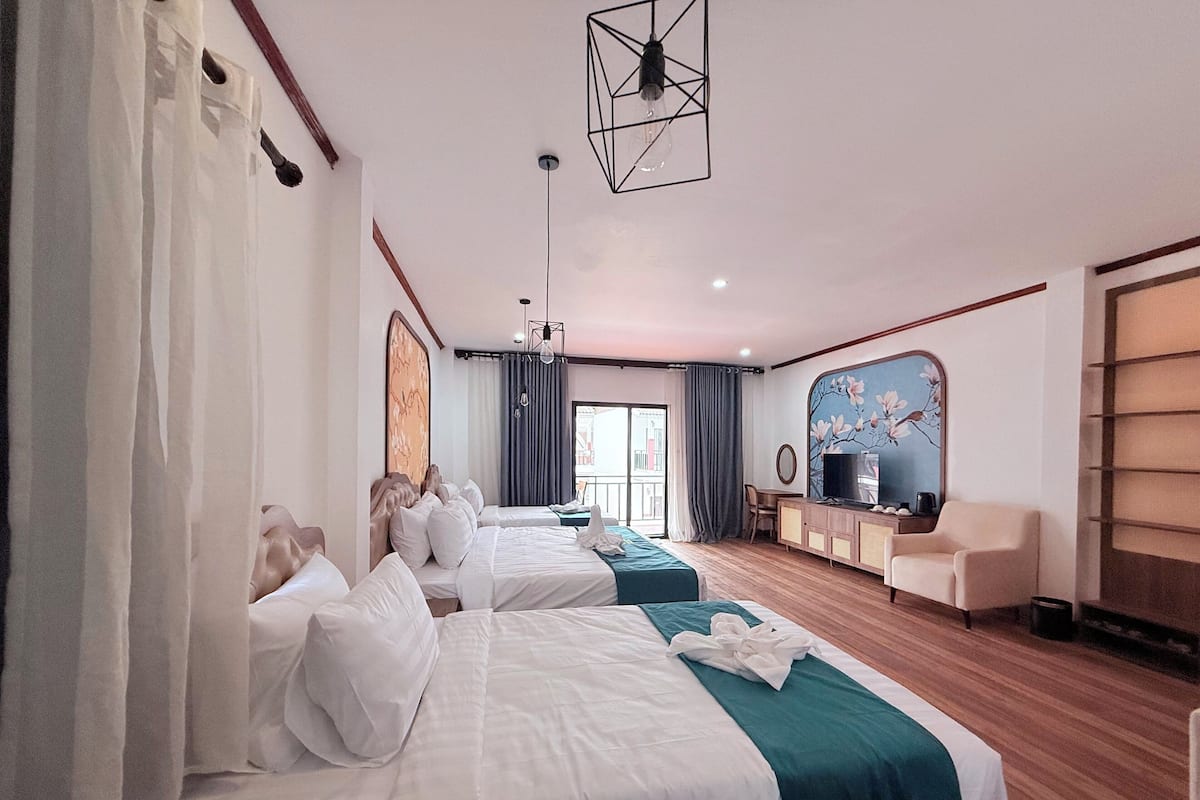 A hotel room with two beds, a TV, a desk, and a large window.