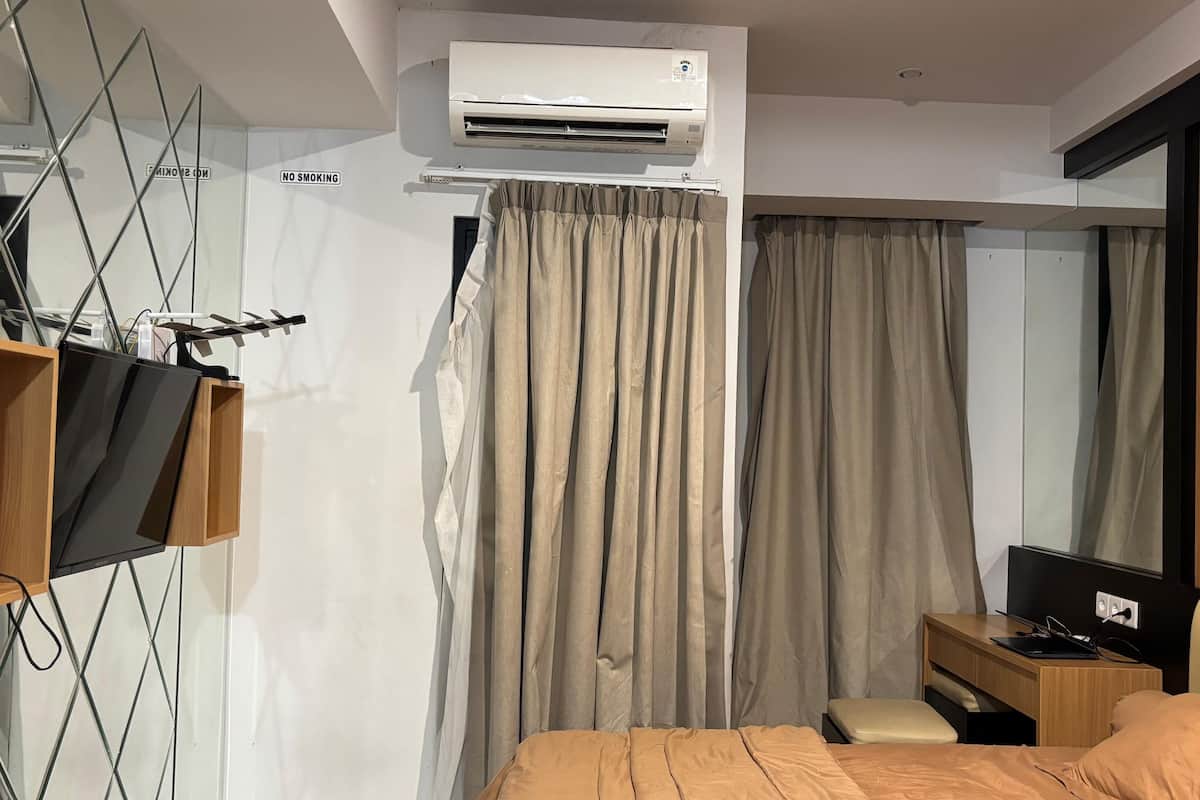 A modern hotel room with a bed, a desk, a TV, and an air conditioning unit.