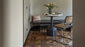 A corner room with a round table, a chair, a vase with flowers, and a pendant light. - Homy® - The Signature Suite 2 (Milan)