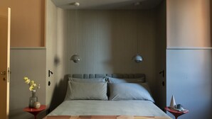 A modern bedroom with a bed, two pendant lights, a small table with a vase of flowers, and a red side table.