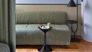 A modern living room with a green sofa, a small black side table with a lamp, and a wooden herringbone floor.