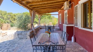Un patio exterior cubierto con mesa y sillas, una planta en maceta y vistas a árboles y colinas.