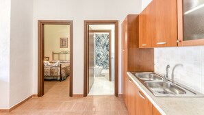 Un pasillo estrecho que conduce a un dormitorio y un baño con inodoro y ducha. Hay una zona de cocina con armarios de madera y un lavamanos.