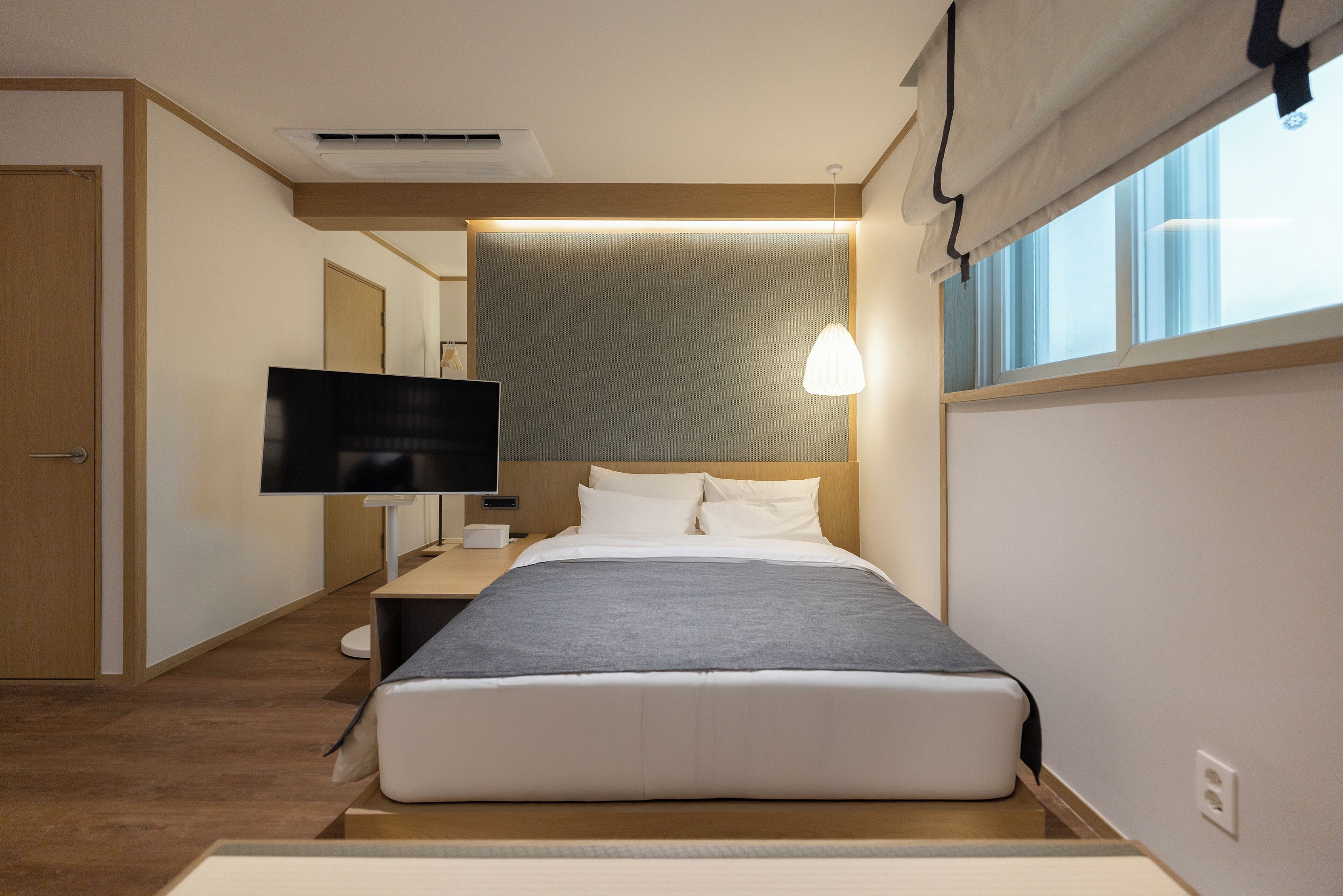 Ein modernes Hotelzimmer mit einem großen Bett, einem Flachbildfernseher, einem Nachttisch und einem Fenster mit Blick.