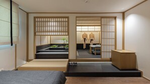 Una habitación de estilo japonés minimalista con suelo de tatami, una cama baja sobre plataforma, una mesita con una silla y un armario de madera.