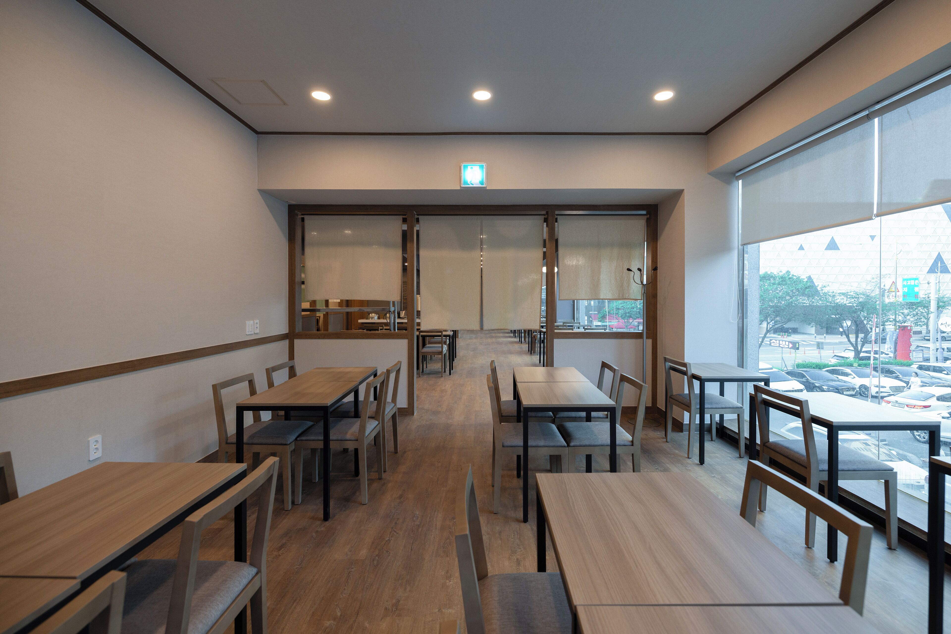 A modern dining area with wooden tables and chairs, large windows with a view of the parking lot.