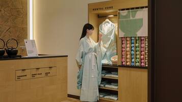 A woman in a traditional dress standing in a room with a wooden counter labeled with tea types.