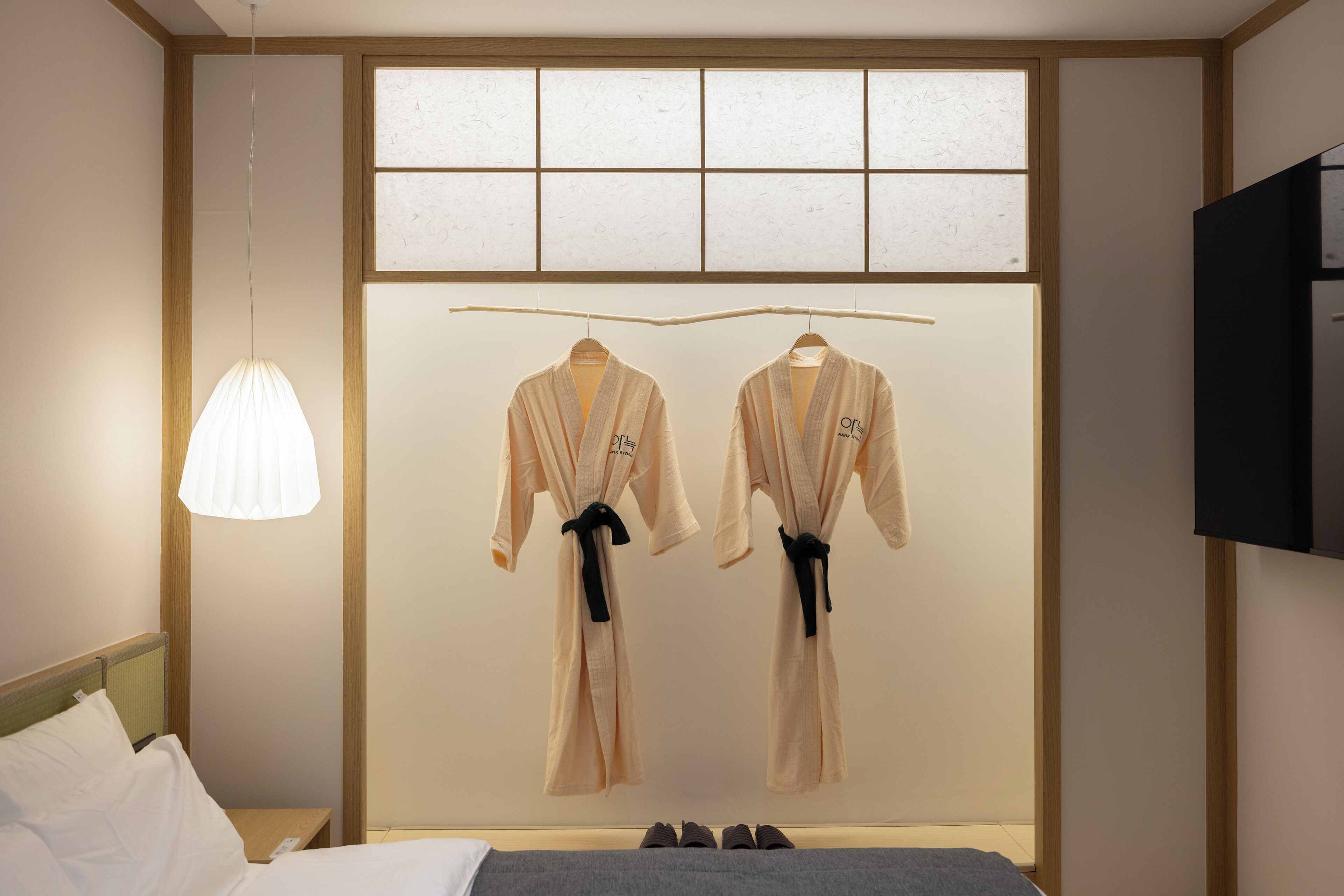 Habitación de hotel con cama, dos batas colgadas en un perchero, televisor y ventana con vistas.
