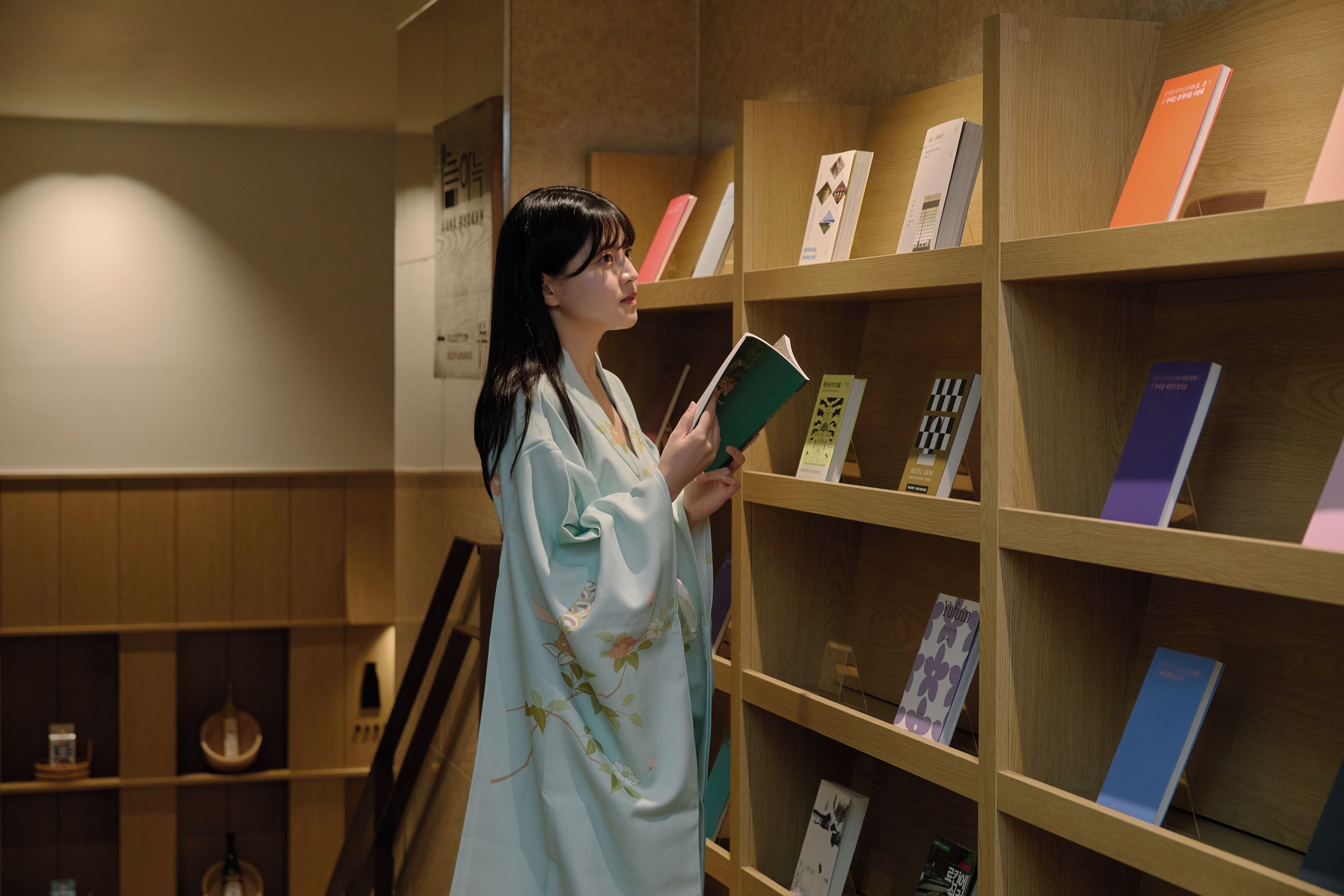 Una persona con bata de estar por casa de pie en una biblioteca con estanterías de madera llenas de libros.