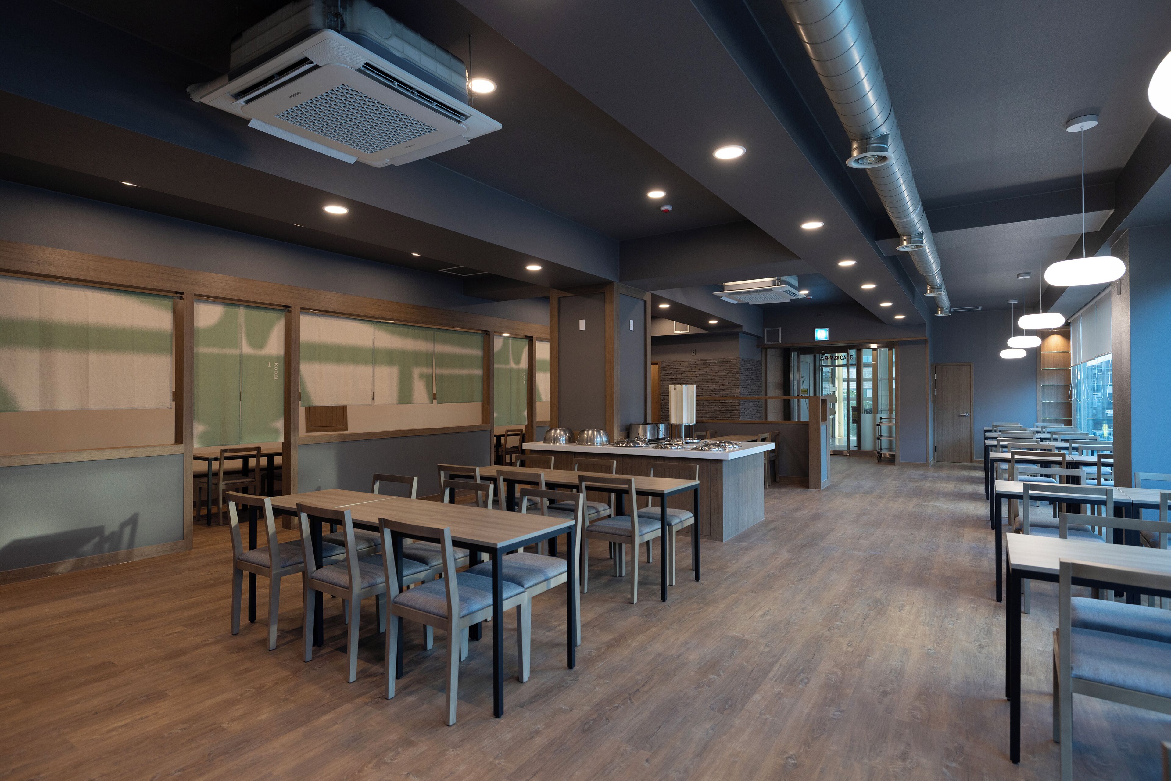 A modern restaurant with wooden tables and chairs, recessed lighting, and a central island.