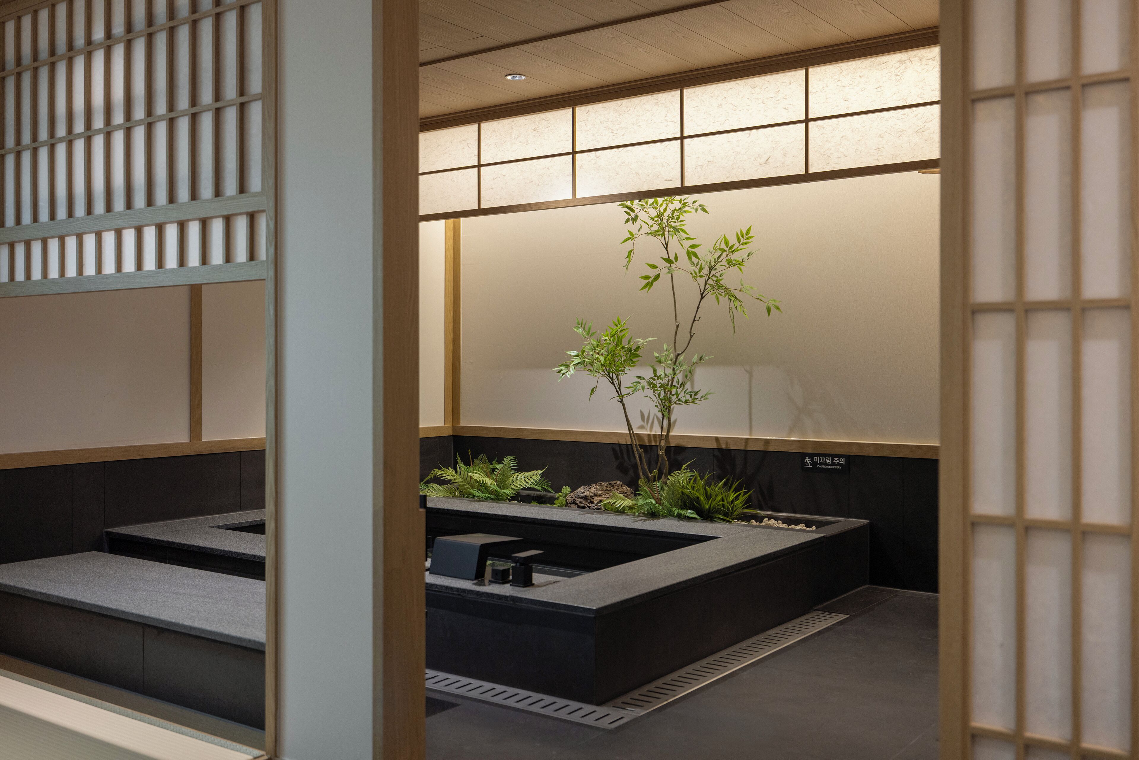 A modern bathroom with a black sink, a small plant, and a tiled floor.