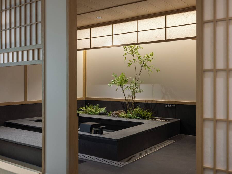 Un baño moderno con un lavabo negro, una planta pequeña y suelo de baldosas.