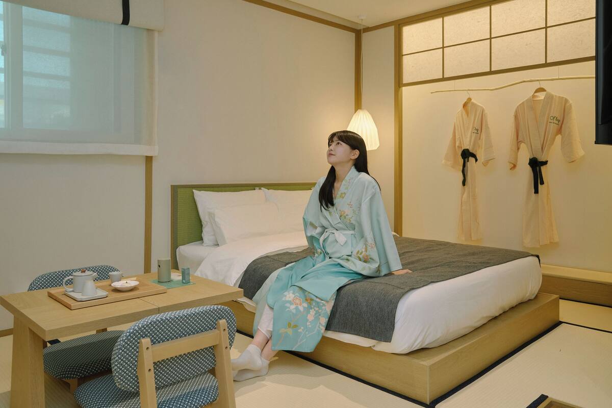 A room with a bed, a table with a teapot and cups, and two chairs.
