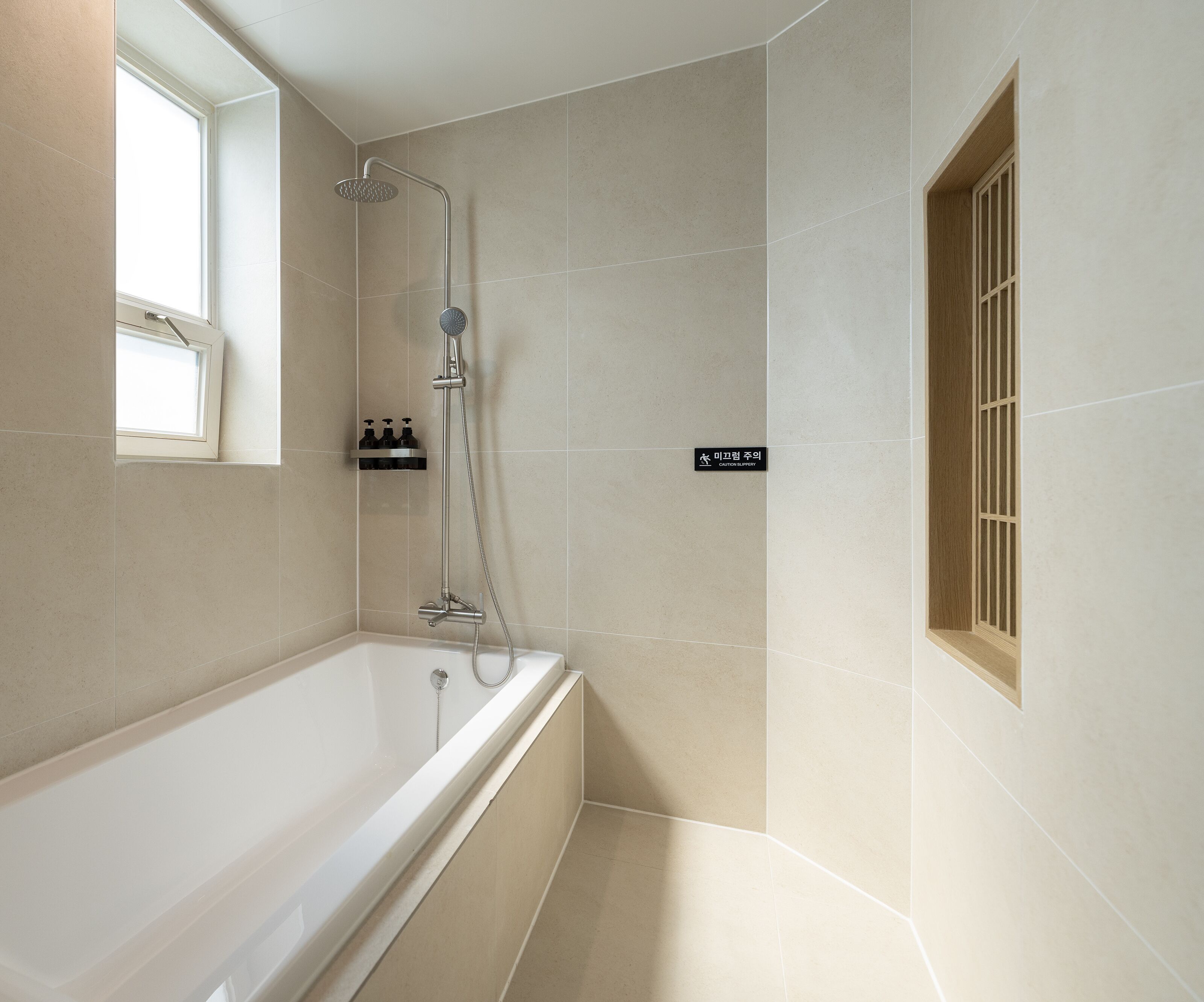 A modern bathroom with a bathtub, a showerhead, and a window.