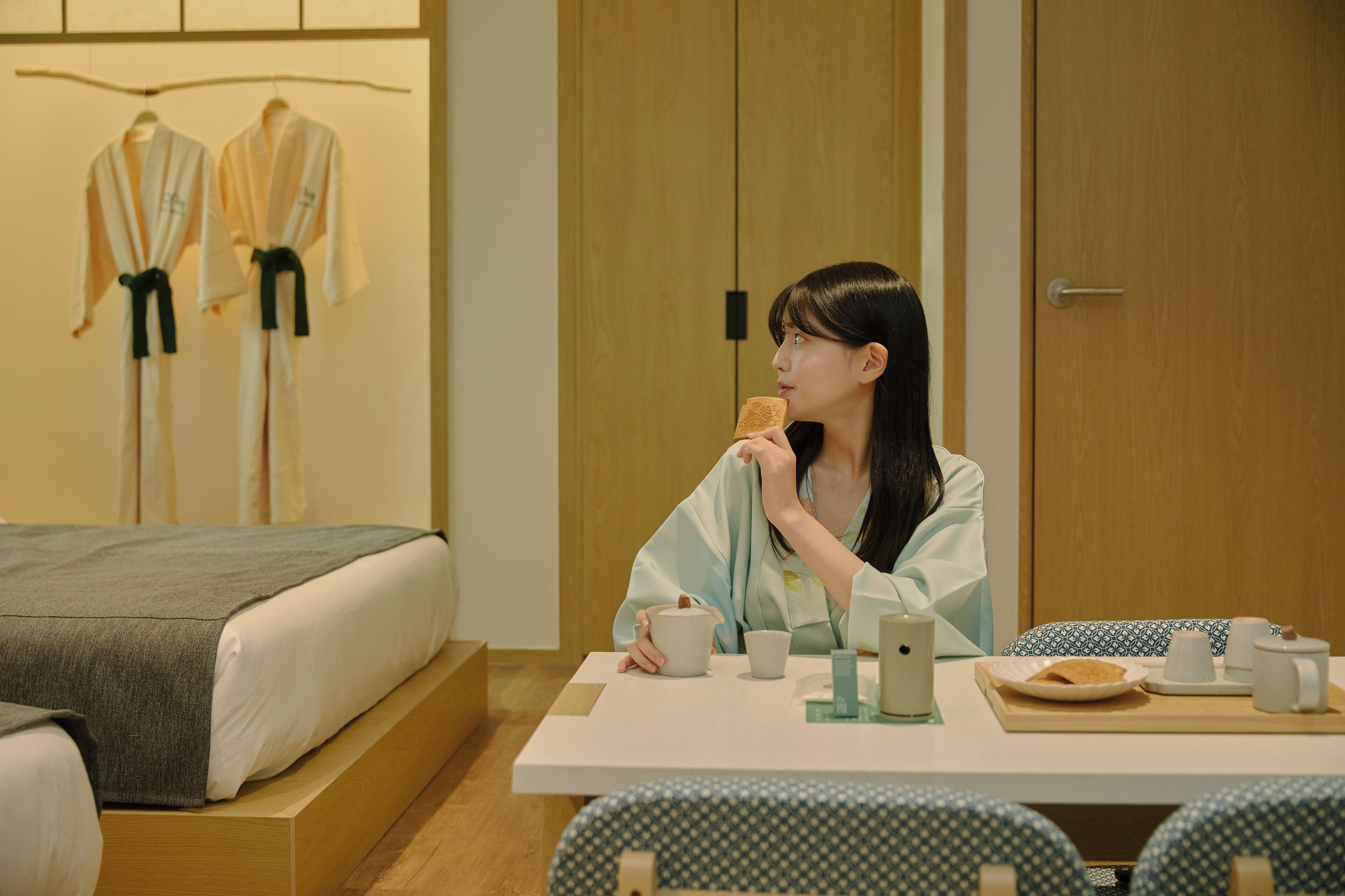 A hotel room with a bed, a table with a tray of food, and a wardrobe in the background.