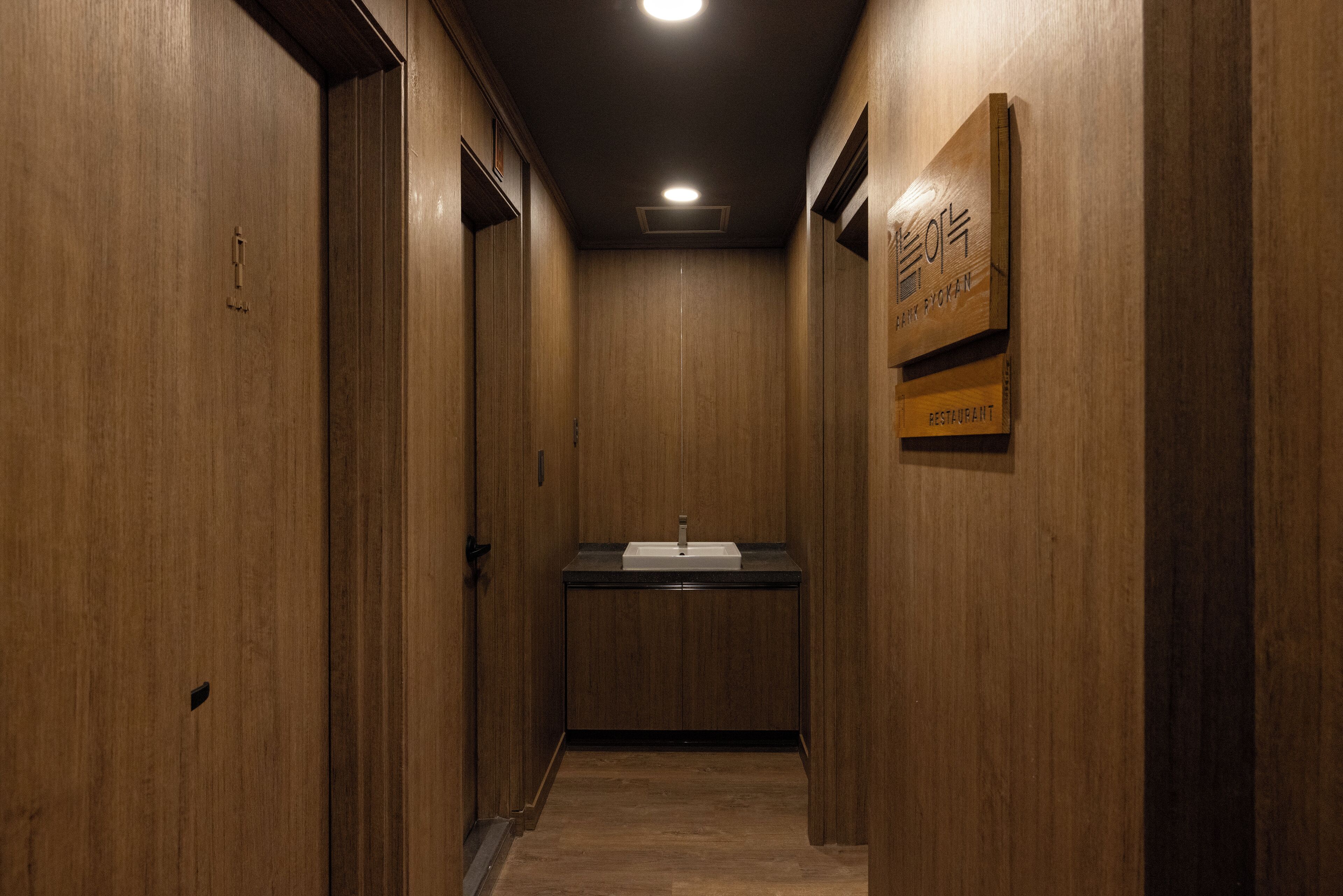 A narrow hallway with wooden walls and a sink in the center.