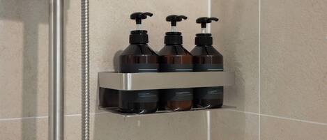Un baño con zona de ducha y estante con tres botellas de champú.