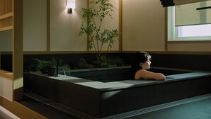 Una habitación tradicional japonesa con suelo de tatami, una mesa de madera baja, una planta de bambú y una ventana con vistas.