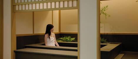 A person sitting on a bench in a room with a low wooden partition and a plant.