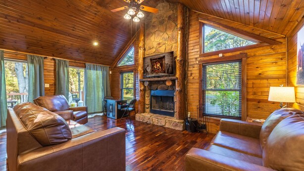 A cozy cabin interior with a stone fireplace, leather sofas, and wooden floors.
