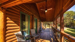 A wooden cabin with a covered porch, two chairs, and a table.