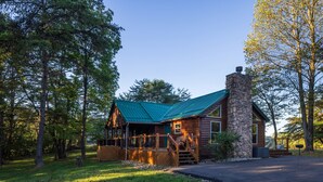A log cabin with a stone chimney, wooden deck, and a covered porch.