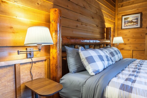 Une pièce de style cabane en bois, avec un lit, deux lampes de chevet et une petite table en bois.