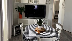 Un comedor con mantel a cuadros, sillas blancas, una planta en maceta y un televisor de pantalla plana montado en la pared.