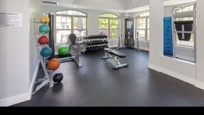Ein großzügiges Fitnesscenter mit Trainingsgeräten, großen Fenstern und einem Deckenventilator.