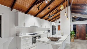 Een moderne keuken met witte kastjes, een groot eiland en een houten plafond.