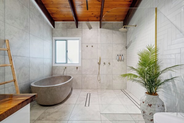 Een moderne badkamer met een vrijstaand bad, een douche en een plant in pot.