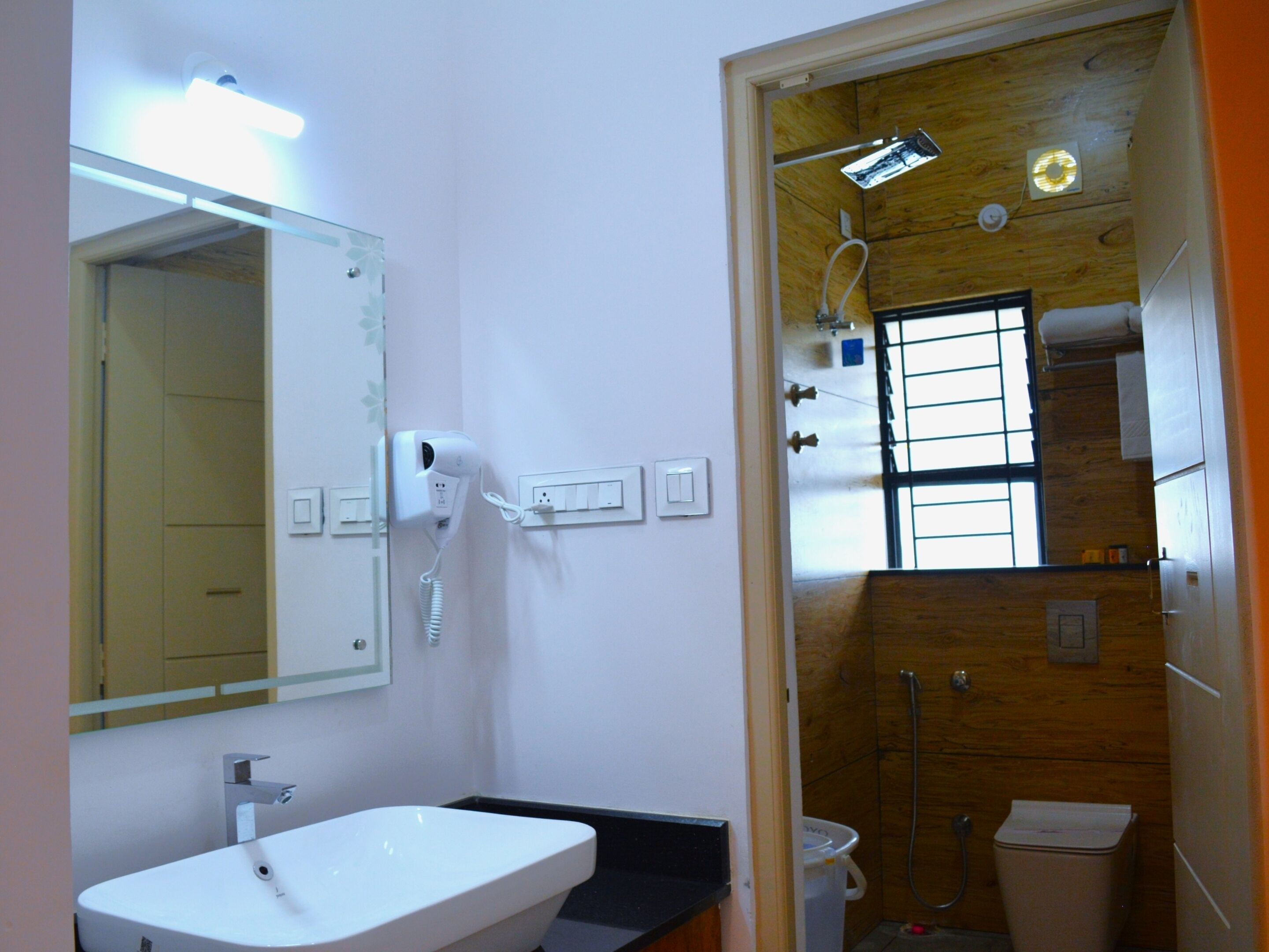 Une salle de bain avec un lavabo blanc, un miroir, un sèche-cheveux, une douche et des toilettes.