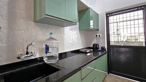 Uma cozinha com bancada preta, armários verdes, um dispensador de água e uma janela com vista para edifícios.