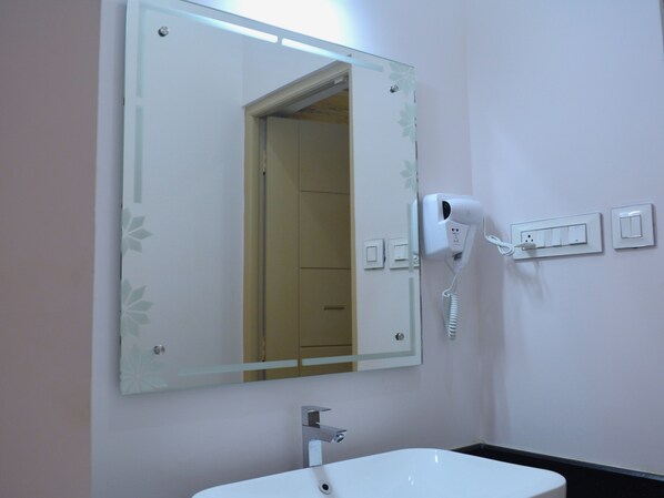 Une salle de bain avec un lavabo blanc, un miroir orné d’un cadre floral, un sèche-cheveux et un interrupteur.
