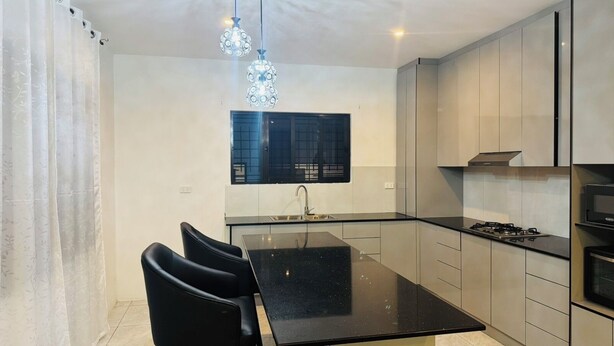 A modern kitchen with a black countertop, stainless steel appliances, and a dining area with black chairs. - Peaceful Nadi Base Retreat (Nadi)