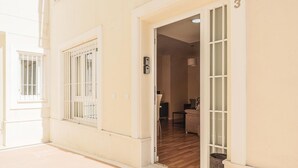 Un pasillo con una puerta que da a una habitación con un sofá y una lámpara. Hay un cubo de basura fuera de la puerta.