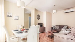 Una sala de estar moderna con comedor, que incluye un sofá, una mesa de centro y una mesa de comedor preparada para cuatro personas.
