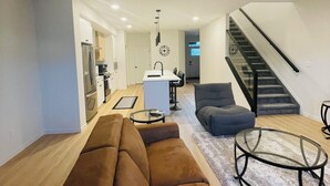 A modern living room with a brown sofa, a glass coffee table, and a staircase leading to an upper floor.