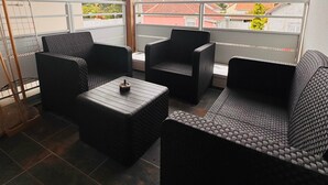 Ein Balkon mit Korbmöbeln, einem Metallgeländer und Blick auf Gebäude und einen Baum.